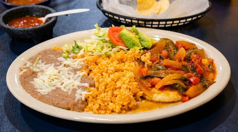 A Mexican dish with refried beans, rice, salad, and a stew of vegetables and chicken.