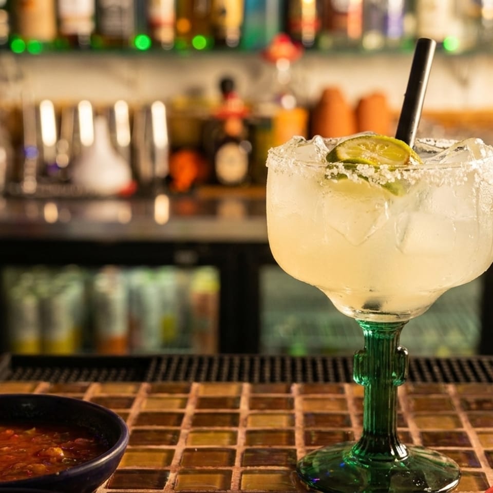 Margarita with lime and salt rim, salsa, and lettuce on a bar counter.