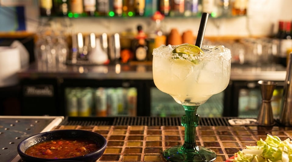 Margarita with lime and salt rim, salsa, and lettuce on a bar counter.