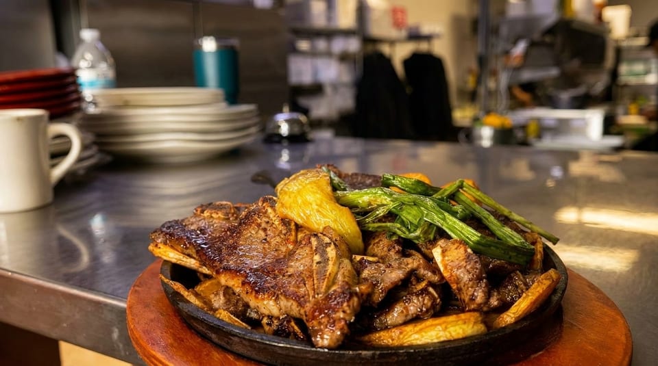 Sizzling steak and vegetables on a cast iron plate in a restaurant kitchen setting.